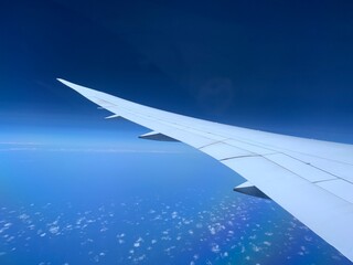Obraz premium White Airplane Wing Flying High Above Blue Ocean and Scattered Clouds