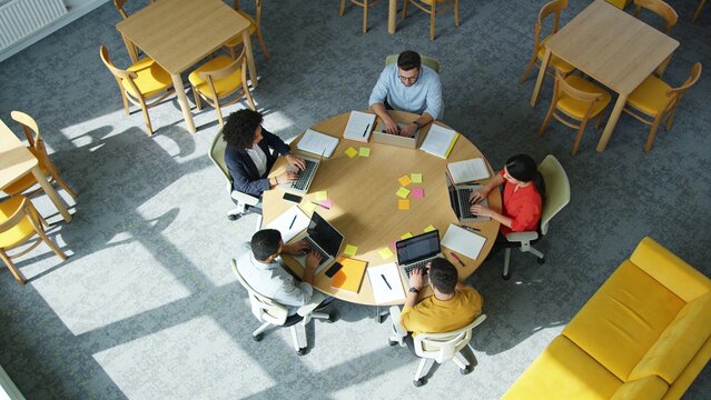 People sit around a table working on laptops in a bright office space