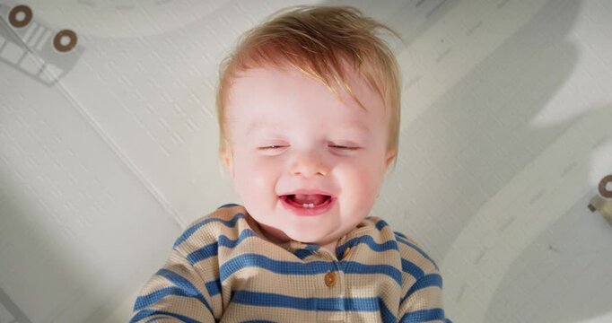 Adorable baby with light hair and blue striped shirt lying on a white patterned mat smiling gently and looking relaxed, captured in close-up shots from two video frames