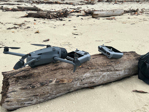 Modern Camera Drone and Remote Controllers Resting on Beach Driftwood
