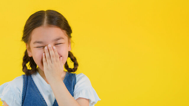 Young Asian Girl Laughing and Covering Her Mouth on Yellow Background