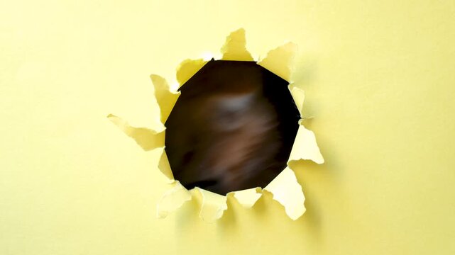 Ginger kitten peeks out of a hole in yellow torn paper close-up.