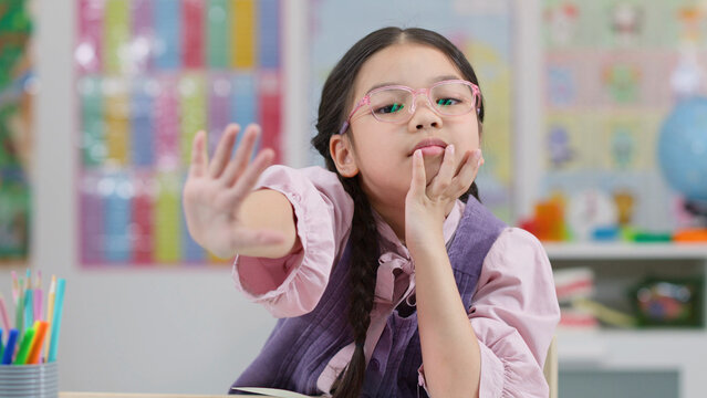 Young East Asian Schoolgirl with Glasses Making Stop Gesture in Classroom