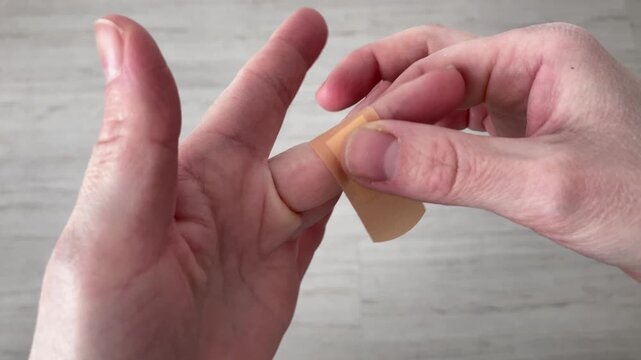 A woman puts a Band-Aid on a small cut on her finger while giving first aid. The patch helps to stop possible bleeding and promotes faster and safer healing. Top view, close up