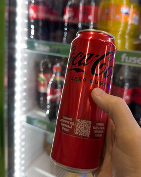Coca-Cola zero sugar can held in a hand near a store refrigerator. It shows branded soft drink choice in retail, Bishkek, Kyrgyzstan