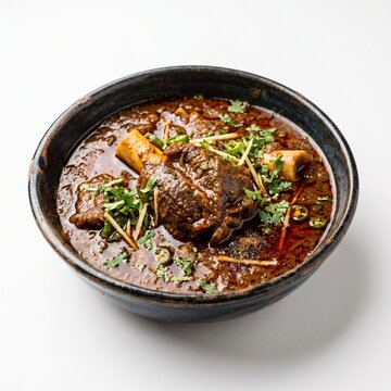 Traditional bowl of spicy mutton nihari garnished with fresh green coriander and ginger strips served in a dark ceramic dish against a clean white studio background