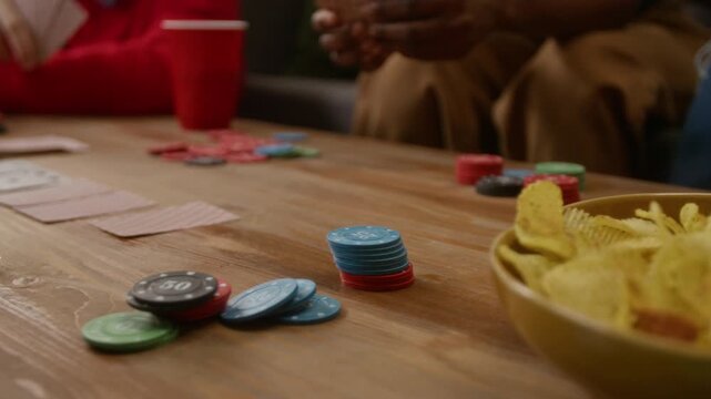 Low angle close up shot of unrecognizable African American woman betting stack of chips while playing poker with friends at table with chips and plastic cups