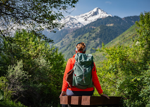 Peaceful moment of female tourist admiring alpine landscape, Back view of hiker with red backpack relaxing during mountain trail, female hiker with a red backpack sits on a wooden bench