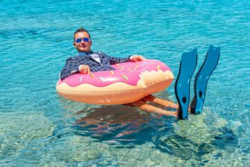 Happy businessman in flippers on an inflatable donut in the sea. © Paopano