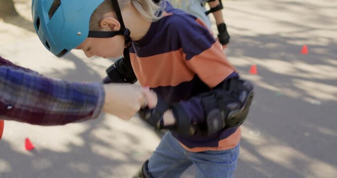 Woman helps boy stand during rollerblade lesson on park path. Child grips hands rising carefully while inline skates stay steady on pavement after small stumble
