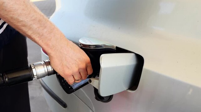 Hand inserting fuel nozzle into car gas tank close up. Refueling automobile at petrol station. Gas pump concept.