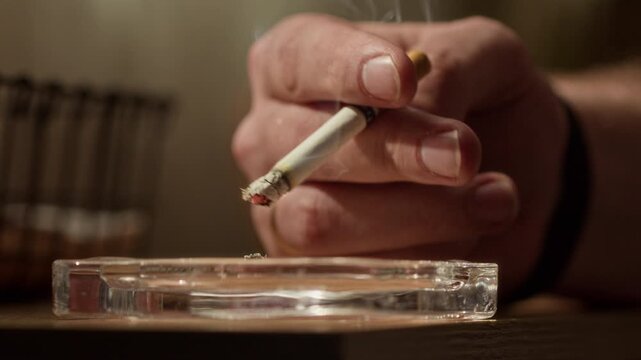 Close up shot of unrecognizable person smoking cigarette and flicking ash into ashtray, mental health awareness background, copy space