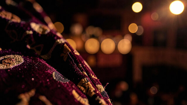 Deep purple velvet fabric texture with gold pattern against warm bokeh lights