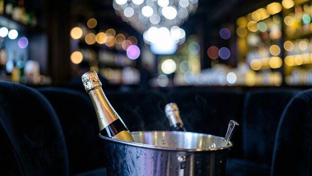 Steam rising from a champagne bottle in a metallic bucket in a dark velvet lounge