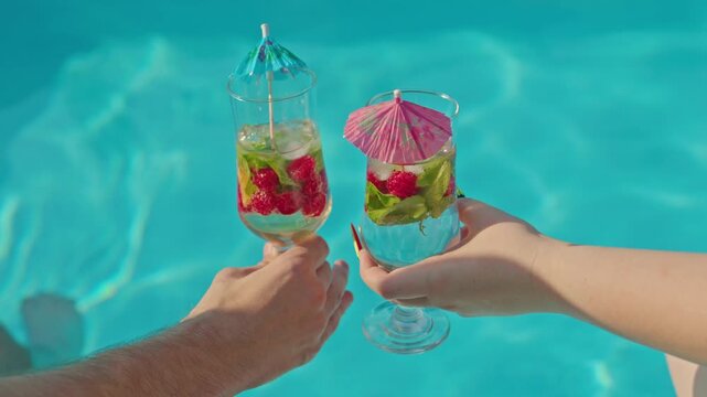 Couple toasting with refreshing raspberry cocktails poolside on sunny summer day.
