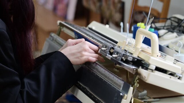 Close up of hands working with blue knitted fabric attached to a flatbed knitting machine