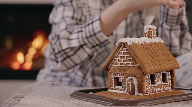 Person decorating a homemade gingerbread house with white icing for christmas.