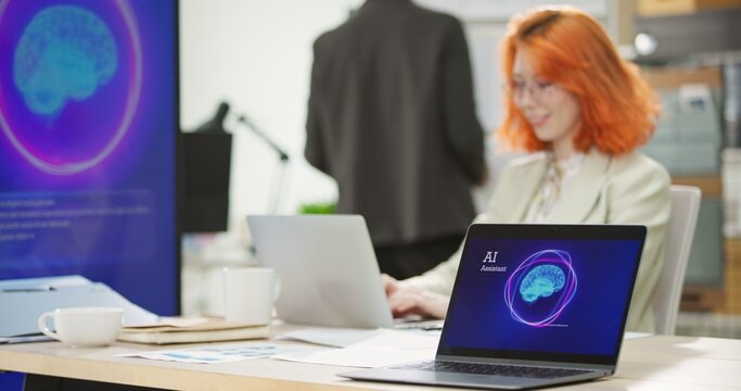 Businesswoman or programmer working on a computer while looking at AI assistant interface on monitor at office. Smart workplace automation, future software engineering, machine learning concept.