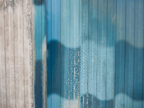 Corrugated metal walls are used for industrial walls or roofs. They have vertical frames, a blue painted surface, and a textured surface with mold.