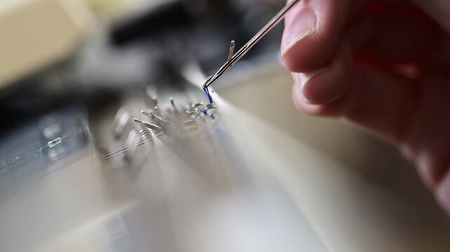 Close up of a woman adjusting blue knitted fabric on a flatbed knitting machine