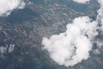 Fototapeta premium Aerial view captures agricultural farmland with geometric field patterns divided by roads and property lines. Fluffy white clouds float above the patchwork landscape of cultivated plots