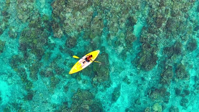 Aerial  view of a woman relaxing on a yellow kayak over a beautiful coral reef in crystal clear turquoise sea water background 	