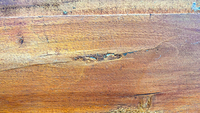 Close-up of a rustic brown wood texture background with natural grain, showing a cracked knot or wood defect filled with resin residue.