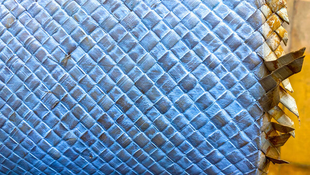 Close-up background texture of a cylindrical hand-woven white rattan basket, showing a detailed cross-hatch pattern and serrated edge design on the side.