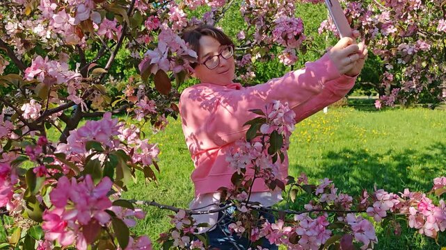 Woman taking selfie with pink blossoms in spring garden. modern lifestyle, social media, capturing nature beauty.