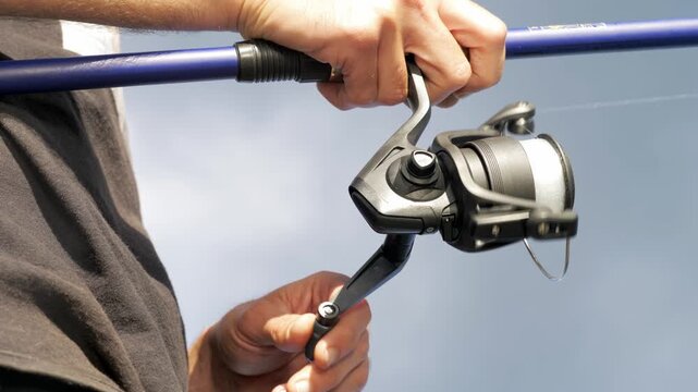 A striking low-angle shot looking up at a fisherman's hands working the reel, with open sky in the background creating a dramatic contrast of light that elevates the cinematic quality.