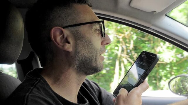 A young man dangerously records a voice message on his smartphone while driving, ignoring traffic rules and putting himself and other road users at serious risk of an accident.