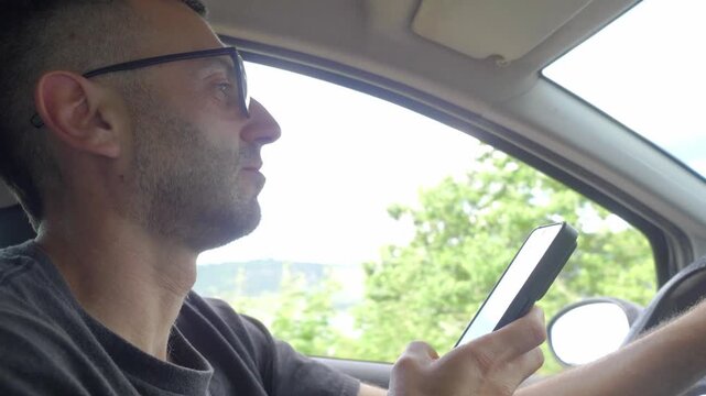 A young man dangerously types a text message on his smartphone while driving, completely distracted from the road, violating traffic laws and risking a serious accident