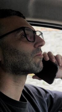 Vertical: Ignoring road safety rules, a young driver holds his phone to his ear while behind the wheel, a reckless and illegal action that significantly raises the chance of a traffic accident.