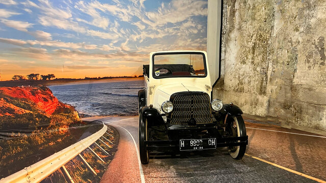 An antique 1920s vintage roadster convertible car displayed with a coastal sunset road backdrop at the Old Transportation Museum in Rasamadu Heritage, Central Java.