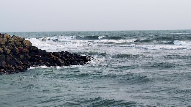 Powerful waves crashing against dark basalt breakwater rocks at Dwarka coast. Perfect for storm, ocean power, coastal India, pilgrimage, and dramatic seascape documentary projects.