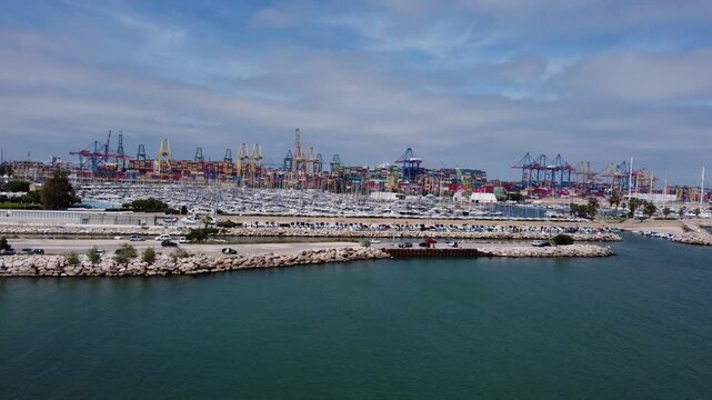 4K aerial drone video advancing and ascending over the mouth of the Turia River in Valencia, Spain. The establishing shot reveals the massive infrastructure of the Port of Valencia, highlighting the l