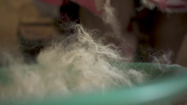 Close-up of wool fibers falling in a bowl, capturing the delicate movement as they rise. Ideal for cultural documentaries or textile industry insights.