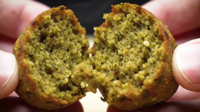 Close up of hands breaking a falafel ball in half revealing texture.