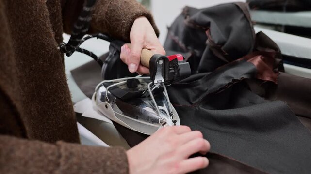 Close up of a tailor using a professional steam iron on black fabric in a fashion workshop