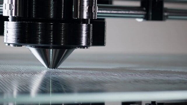3D printer nozzle precisely extrudes filament onto a glass surface, showcasing the layering process in a well-lit indoor workspace with modern equipment