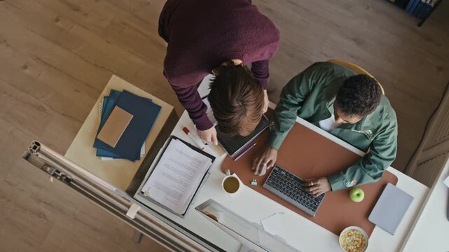 Top view of two male colleagues taking seats and starting daily office tasks with paperwork and digital devices in modern workspace