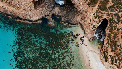 Obraz premium Landscape cinematically edited aerial drone shot Birds Eye view over the blue lagoon coast, malta with clear blue turquoise Mediterranean Sea water and limestone cliffs and green foliage in summer
