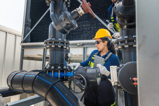 Engineers checking piping infrastructure at plant, Skilled workers performing maintenance on industrial plumbing and cooling tower, Technician team operating water valve in industrial cooling system