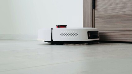 Robotic vacuum cleaner navigating smooth floor near door threshold with contemporary design