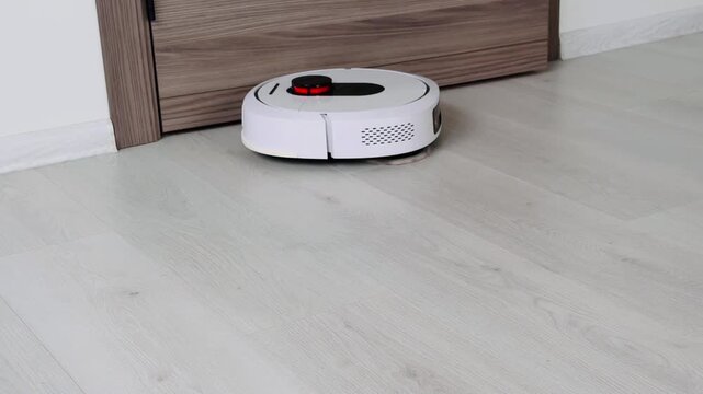 Robot vacuum cleaner navigating across smooth white laminate flooring near wooden door edge