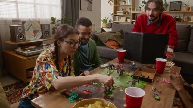 Young adult woman throwing dice and making move while playing RPG tabletop game with friends in cozy living room