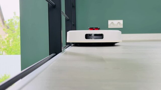 Robot vacuum cleaner cleaning along a metal staircase railing on a light gray second floor