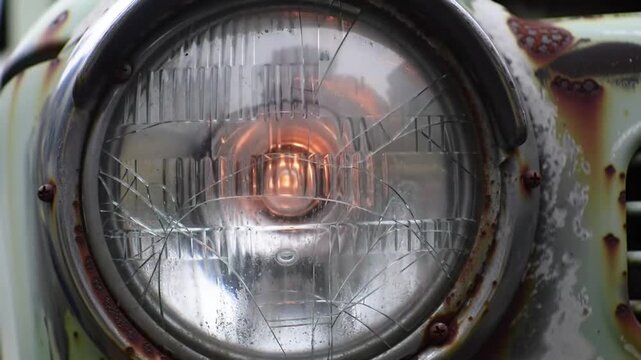 Close-up of a vintage car headlight with cracked glass and rust.