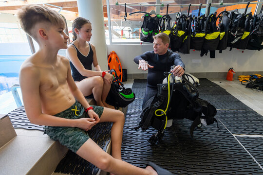 Diving instructor explaining scuba equipment with an oxygen cylinder to a boy and a girl during a pool lesson
