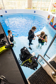 Scuba diving instructor helping a teenage boy adjust his equipment in an indoor swimming pool
